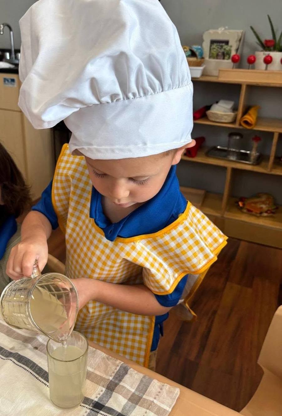 A child in a chef hat carefully pours lemonade into a glass