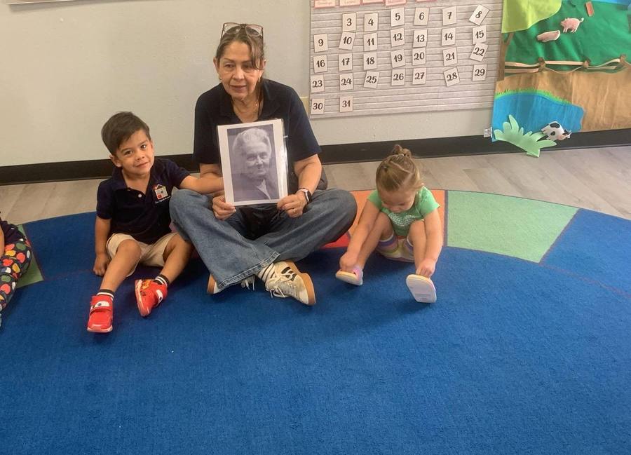 A guide holds a portrait of Maria Montessori while a toddler puts on her own shoes